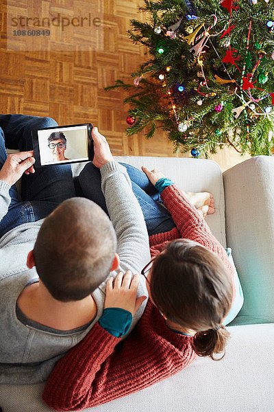 Draufsicht auf das Paar  das zu Weihnachten auf dem Sofa sitzt und einen digitalen Tablet-Videoanruf macht