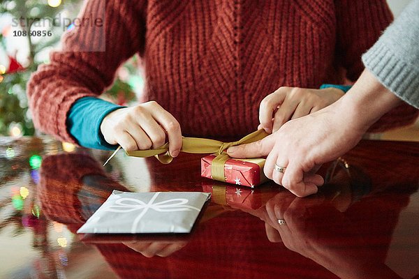 Ausschnittaufnahme der Hände des Paares beim Einpacken des Weihnachtsgeschenks bei Tisch