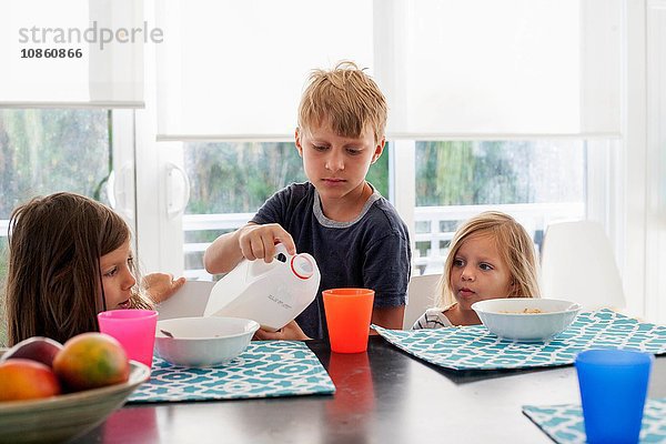 Großer Bruder gießt Milch in den Plastikbecher der Schwestern