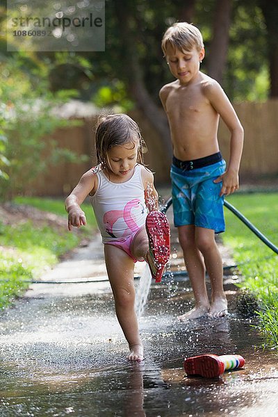 Kind in Gummistiefeln spielt in Wasserpfütze  Bruder schaut zu