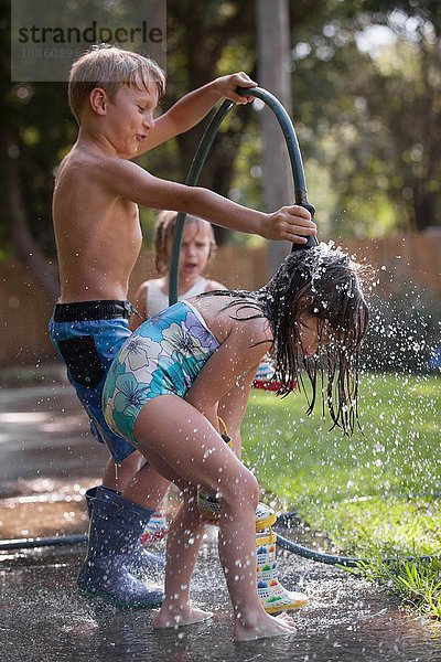 Kinder spielen mit Wasserschlauch auf dem Bürgersteig