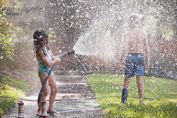 Kinder spielen mit Wasserschlauch auf dem Bürgersteig