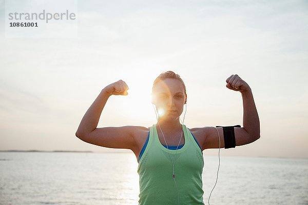 Frau trägt Aktivitäts-Tracker  Arme hochgehoben  Muskeln beugen und in die Kamera schauen