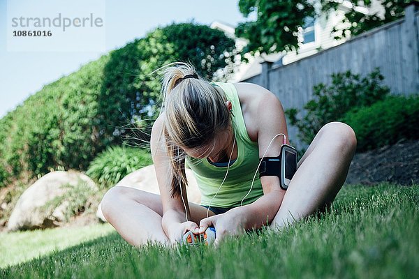 Frau mit Aktivitätsspürgerät auf Gras sitzend  sich streckend und nach unten blickend