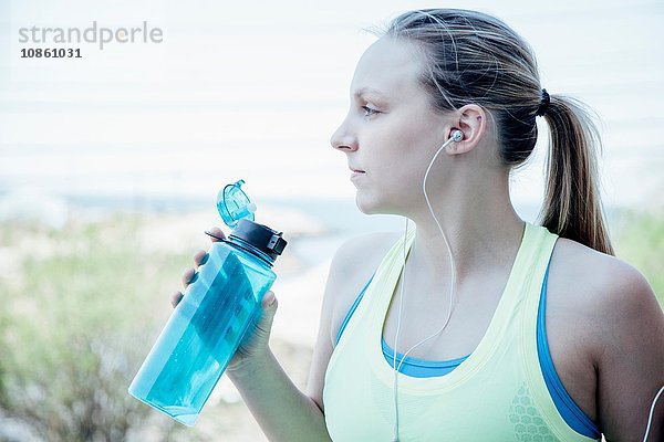 Frau mit Ohrstöpseln hält Plastik-Wasserflasche und schaut weg