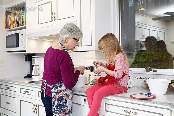 Mädchen und Großmutter schauen in den Kochtopf an der Küchentheke
