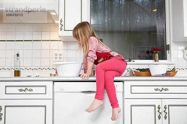 Mädchen schaut in die Rührschüssel  während sie auf der Küchentheke sitzt