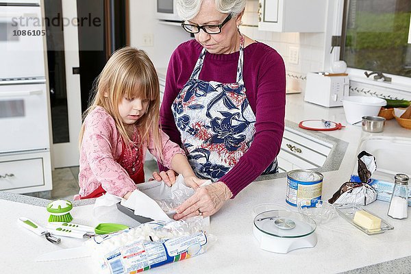 Mädchen und Großmutter beim Backen von Backpapier im Backblech