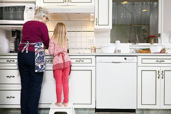 Rückansicht von Mädchen und Großmutter am Küchenherd stehend