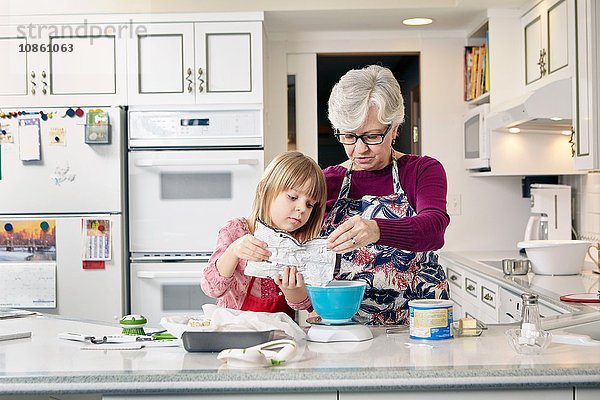 Mädchen und Großmutter gießen Kuchenmischung an der Küchentheke