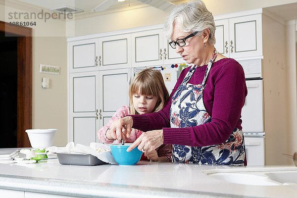 Mädchen und Großmutter mischen Kuchen an der Küchentheke