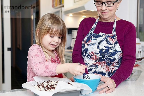 Mädchen quirlt mit Großmutter Kuchen an der Küchentheke