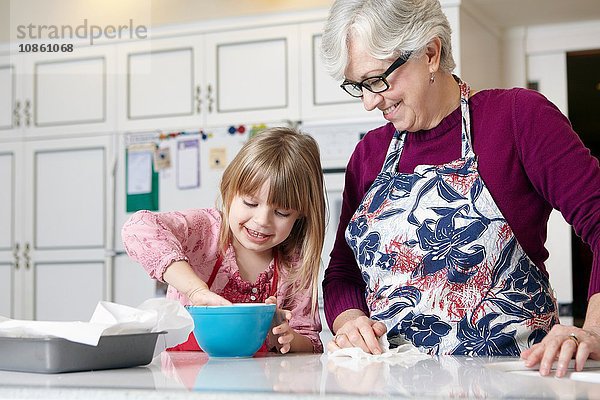 Mädchen und Großmutter mischen Kuchen in einer Schüssel an der Küchentheke