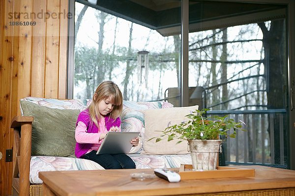 Mädchen sitzt auf Wohnzimmer-Sofa und benutzt Touchscreen auf digitalem Tablet