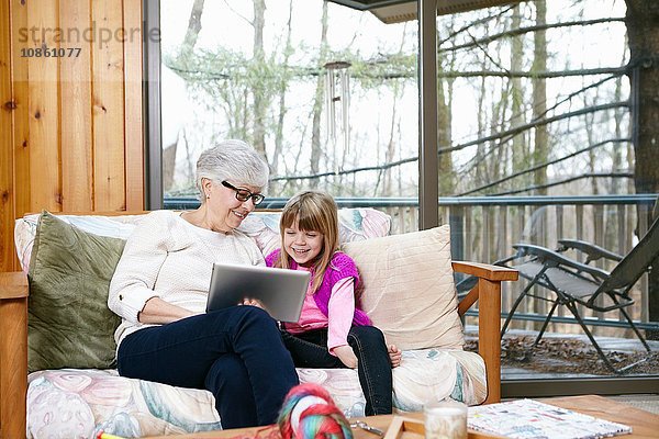 Ältere Frau und Enkelin durchsuchen digitales Tablet auf Wohnzimmersofa