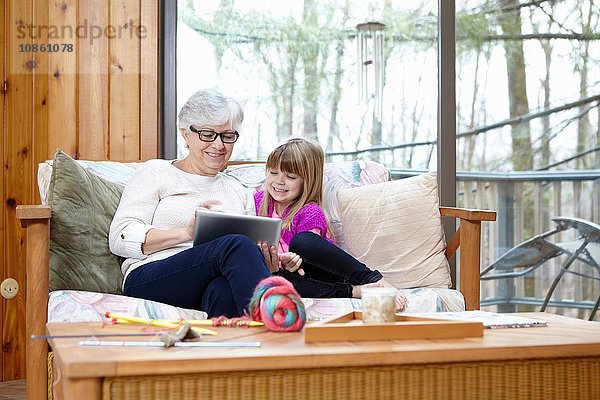 Ältere Frau und Enkelin benutzen digitales Tablet auf Wohnzimmersofa