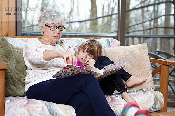 Ältere Frau liest Enkelin auf Wohnzimmersofa Geschichte vor
