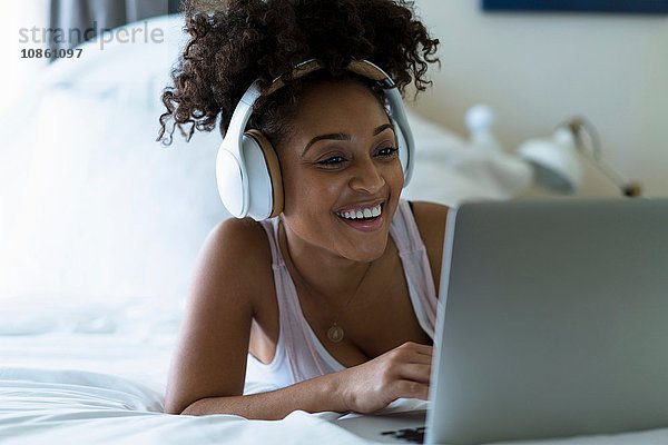 Frau im Schlafzimmer  benutzt Laptop  trägt Kopfhörer