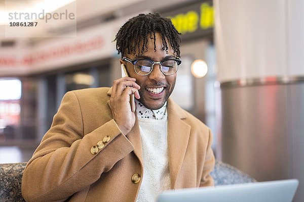 Junger Geschäftsmann sitzt im Bahnhof und spricht über Smartphone