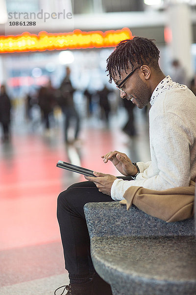 Junger Mann sitzt im Bahnhof und benutzt digitalen Tablet-Touchscreen