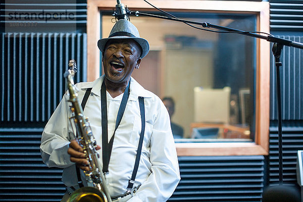 Männlicher Musiker im Aufnahmestudio  Saxophon haltend  lachend