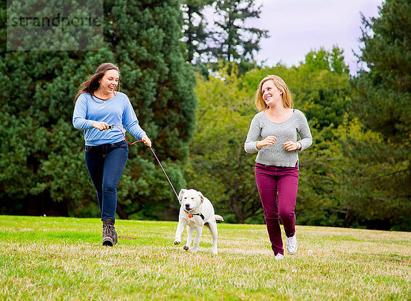 Zwei junge Frauen rennen mit Hund im Park