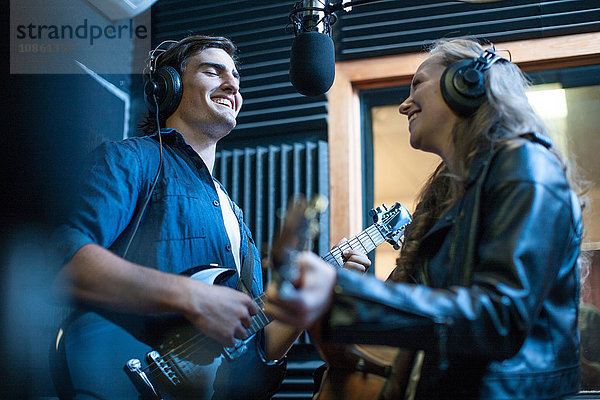 Zwei Musiker im Aufnahmestudio  singen ins Mikrofon und spielen Gitarre