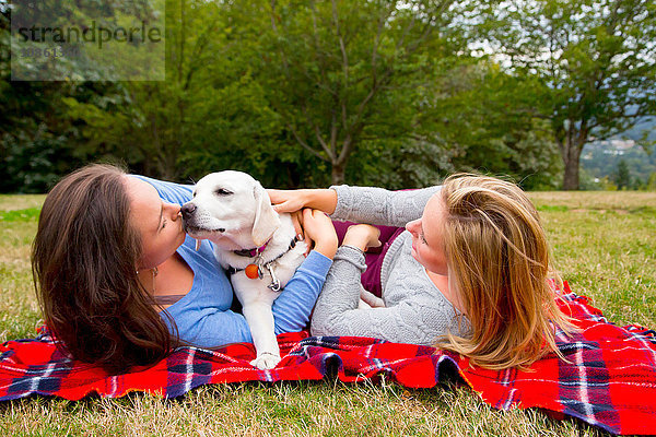 Zwei junge Frauen mit Haushund  auf einer Decke liegend im Park