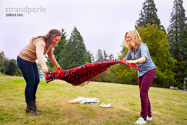 Zwei junge Frauen legen im Park eine Picknickdecke aus