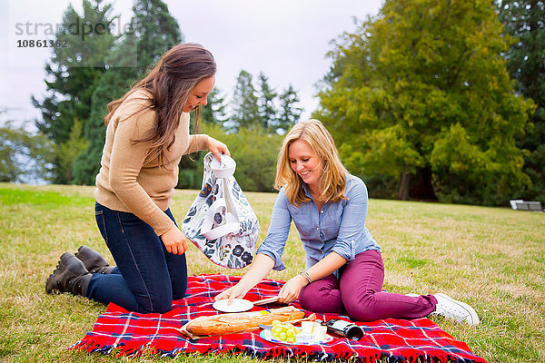 Zwei junge Frauen machen ein Picknick auf einer Decke im Park