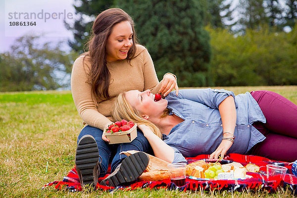 Junge Frau füttert Freundin mit Erdbeeren  im Park