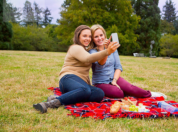 Zwei junge Frauen beim Picknick im Park  beim Selfie  mit dem Smartphone