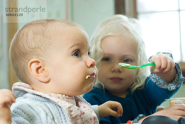 Junges Mädchen füttert kleine Schwester mit Löffel