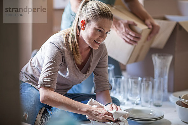 Umzug: Frau wickelt Glaswaren vor dem Verpacken in Papier ein
