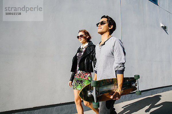 Junges Paar geht gemeinsam im Freien spazieren  Mann trägt Skateboard