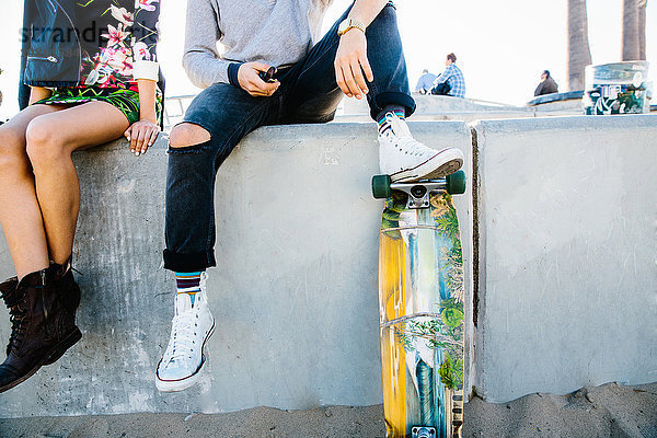 Junges Paar sitzt an der Wand  Mann ruht mit dem Fuß auf dem Skateboard  niedriger Abschnitt