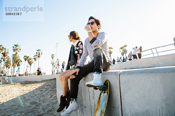 Junges Paar sitzt an der Wand  Mann ruht mit dem Fuß auf dem Skateboard