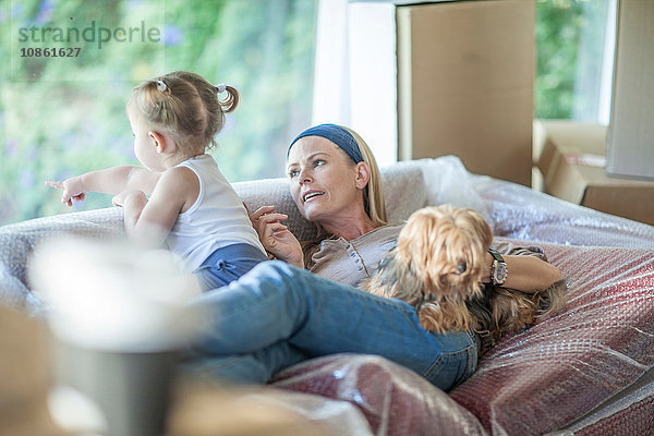 Umzug: Muttertochter und Haushund entspannen sich auf einem Sofa mit Luftpolsterfolie