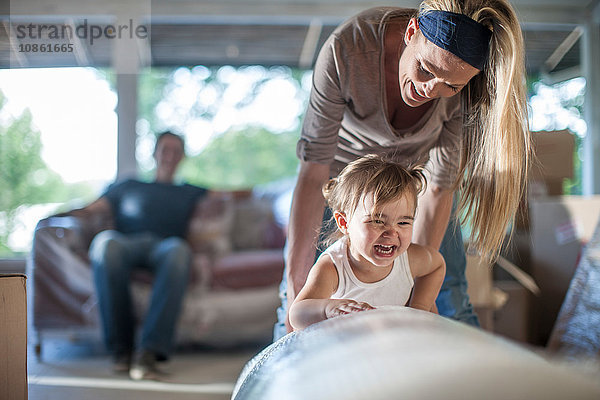 Umzug: Mann sitzt auf einem Sofa mit Luftpolsterfolie  Frau spielt mit ihrer Tochter