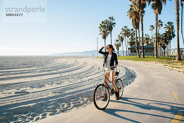 Junge Frau radelt am Strand mit Blick aufs Meer  Venice Beach  Kalifornien  USA