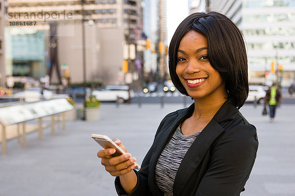 Porträt einer Geschäftsfrau  Smartphone in der Hand  lächelnd  im Freien