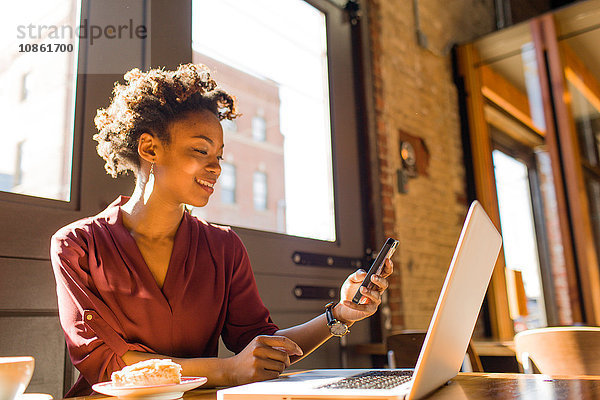 Junge Geschäftsfrau sitzt im Cafe und benutzt Laptop und Smartphone