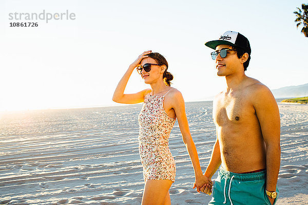 Junges Paar im Badeanzug und in Shorts am Strand spazieren  Venice Beach  Kalifornien  USA
