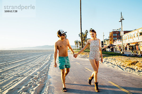Junges Paar im Badeanzug und in Shorts am Strand spazieren  Venice Beach  Kalifornien  USA