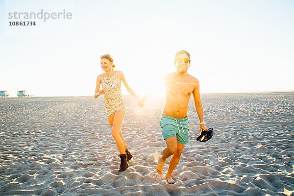 Junges Paar läuft in Badehose und Shorts am sonnenbeschienenen Strand  Venice Beach  Kalifornien  USA