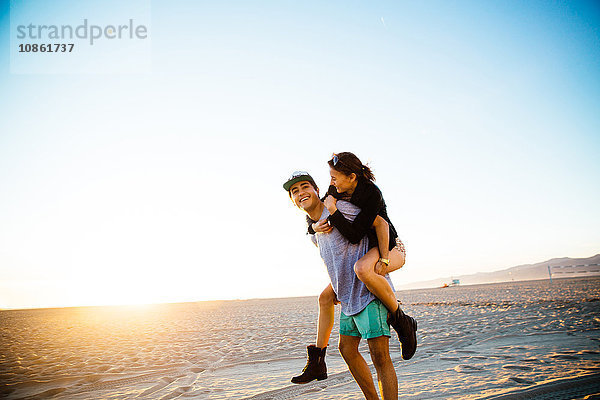 Junger Mann schenkt seiner Freundin ein Huckepack am Strand  Venice Beach  Kalifornien  USA