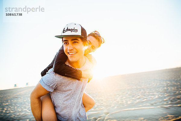 Junger Mann gibt seiner Freundin ein Huckepack am sonnigen Strand  Venice Beach  Kalifornien  USA