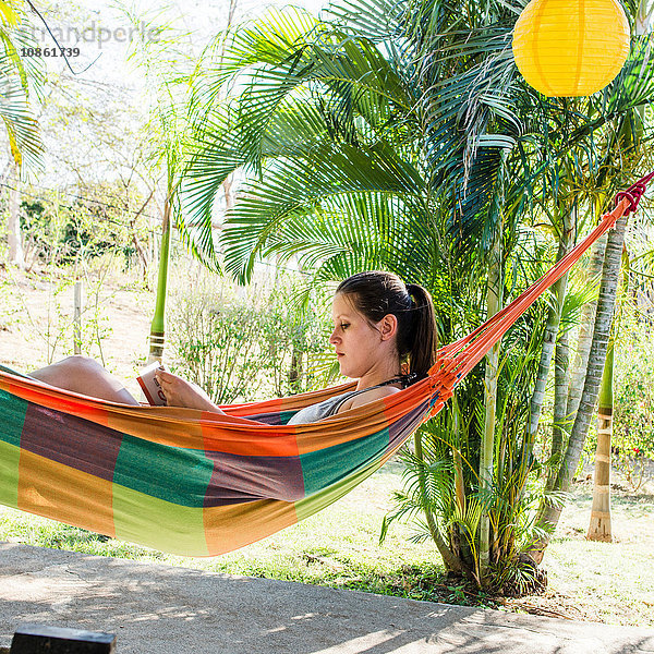 Junge Frau liest in der Hängematte liegend ein Buch  Tamarindo  Guancaste  Costa Rica