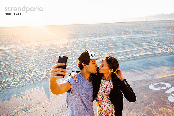 Junges Pärchen  das sich für Smartphone-Selfie am Strand zusammenrauft  Venice Beach  Kalifornien  USA