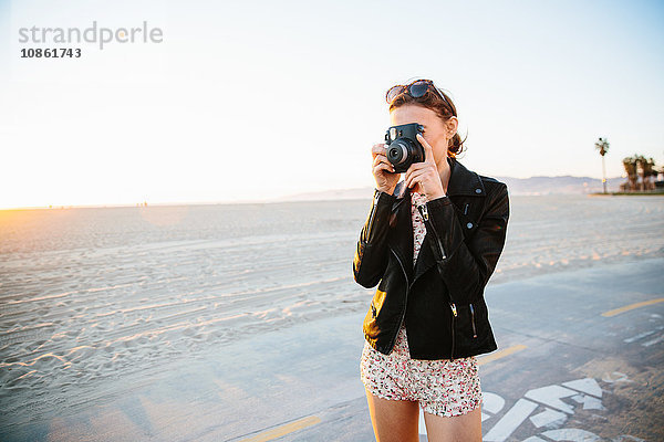 Junge Frau fotografiert mit Sofortbildkamera am Strand  Venice Beach  Kalifornien  USA